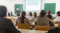 Föreläsningssal på universitet med studenter i förgrunden och en lärare vid tavlan.