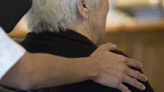 Detalj - hand på äldre kvinnas rygg på äldreboende.