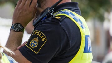 Detalj polis med uniform som pratar i mobil. Man ser arm och tröja med polisens emblem.