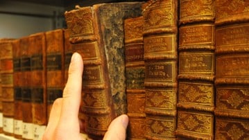 Hand som drar ut en gammal bok från en bibliotekshylla.