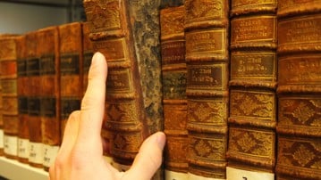 Hand som drar ut en gammal bok från en bibliotekshylla.