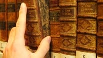 Hand som drar ut en gammal bok från en bibliotekshylla.