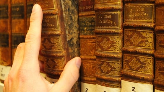 Hand som drar ut en gammal bok från en bibliotekshylla.