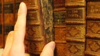 Hand som drar ut en gammal bok från en bibliotekshylla.