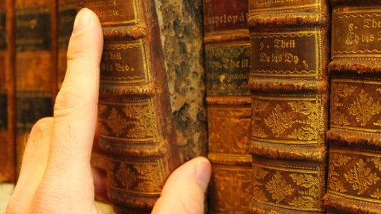 Hand som drar ut en gammal bok från en bibliotekshylla.