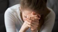 Kvinna som inte mår bra sitter lutad framåt med händerna knäppta framför ansiktet.