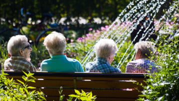 Fyra äldre kvinnor sitter på en parkbänk och samtalar.
