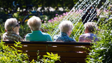 Fyra äldre kvinnor sitter på en parkbänk och samtalar.