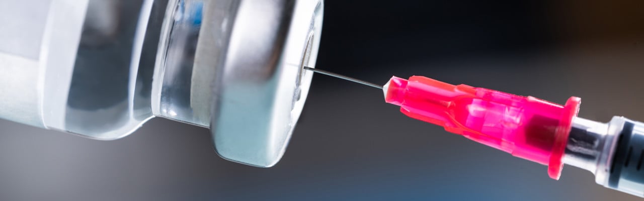 Nål som sticks in i behållare med vaccin.