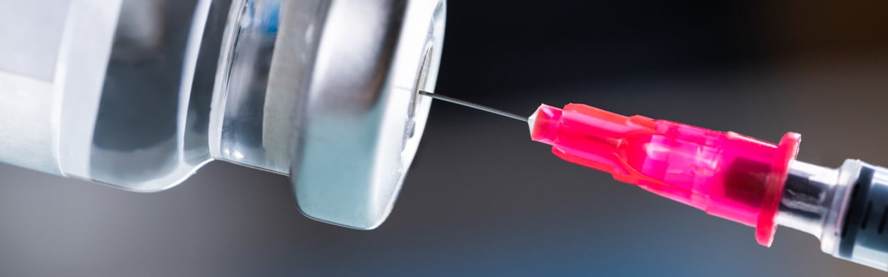Nål som sticks in i behållare med vaccin.