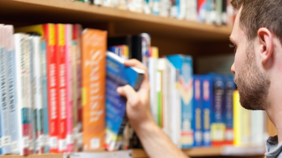 Yngre man väljer ut en bok ur bokhyllan på ett bibliotek.