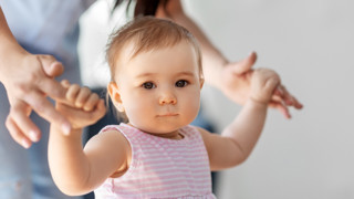 Liten flicka lär sig gå med hjälp av sin mamma.
