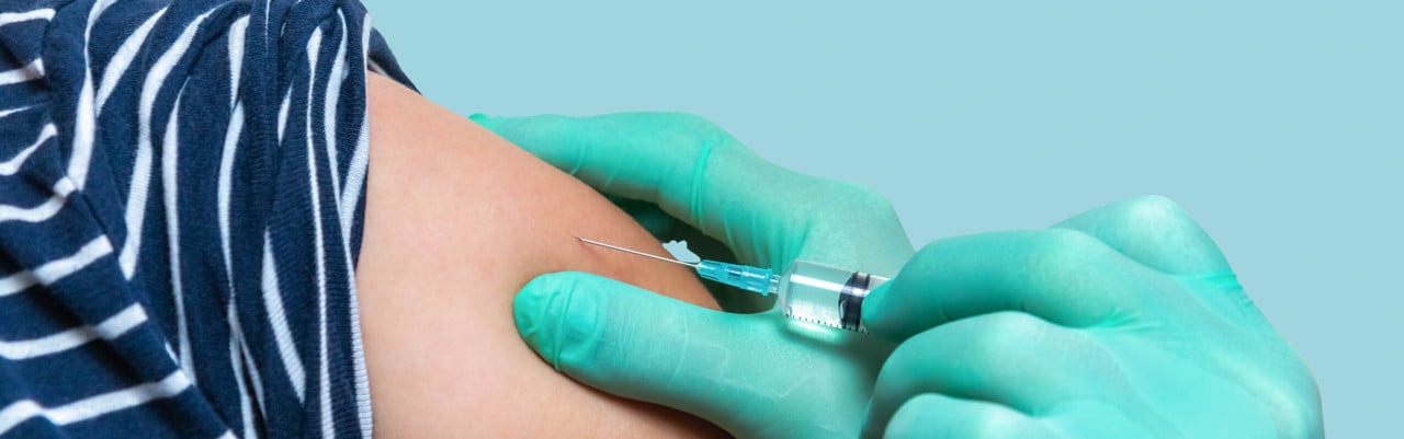 Handskbeklädda händer ger spruta med vaccin på en arm.