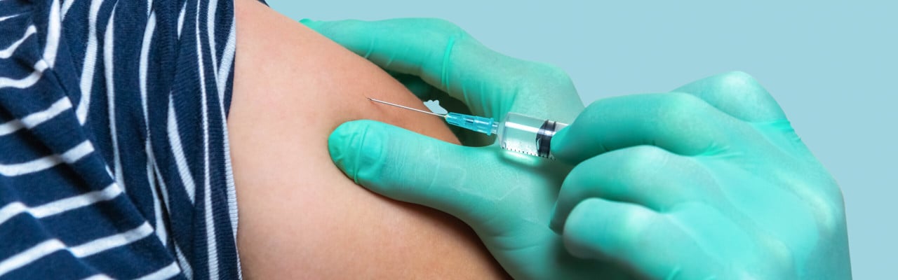 Handskbeklädda händer ger spruta med vaccin på en arm.