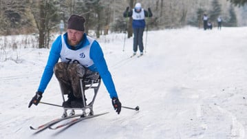 Funktionshindrad person åker skidor med hjälpa av en speciell skidkälke.
