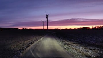 Vindkraftverk i tidig gryning och en bilväg.