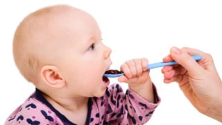 Hand som matar baby med sked.