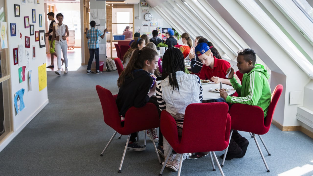 En grupp skolelever på högstadiet sitter vid ett bord och äter mat.
