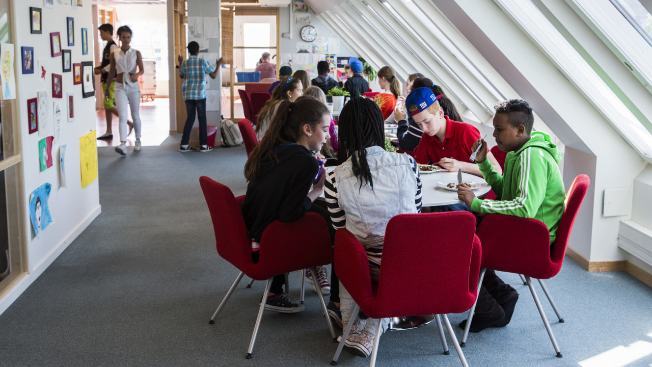 En grupp skolelever på högstadiet sitter vid ett bord och äter mat.