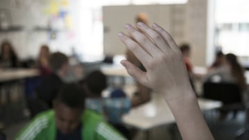 Närbild på hand på skolbarn som räcker upp handen i klassrummet.