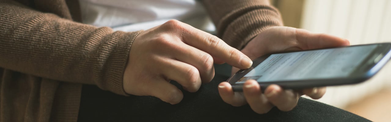 Detalj på person vars händer håller i en mobiltelefon som hen surfar på.