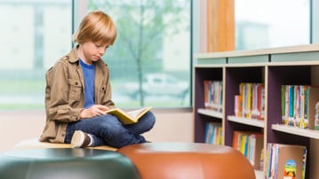 Pojke läser bok i ett bibliotek.