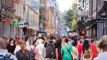 Sommardag på gågatan Drottninggatan mellan Mäster Samuelsgatan och Kungsgatan i Stockholm, Sverige, med folk i rörelse.