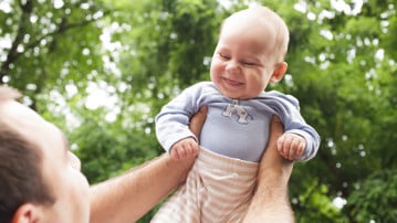 Pappa som håller upp sin baby i luften. Babyn skrattar.