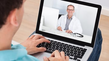 En person pratar med sin doktor hemifrån via datorn.