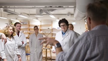Pepole in lab coats listening to a male professor