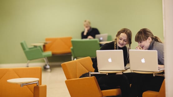 Två glada studenter som skriver på sina datorer.