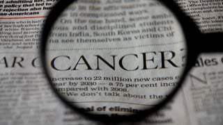 Närbild på ett förstoringsglas som visar ordet Cancer från en tidningstext