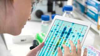 Bild på person i labb som läser av DNA-sekvens på ipad
