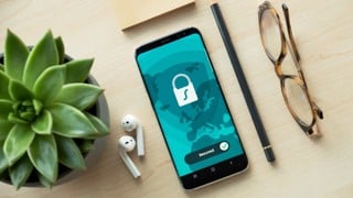 En mobiltelefon ligger på ett bord bredvid en krukväxt, hörlurar och en penna. Mobilens display visar ett hänglås och texten "secured".