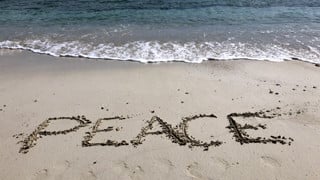 Bild på sandstrand där någon skrivit "Peace" i sanden. Illustrerar freds- och konfliktstudier.
