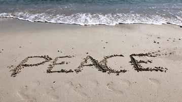 Bild på sandstrand där någon skrivit "Peace" i sanden. Illustrerar freds- och konfliktstudier.