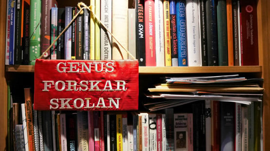 Broderad skylt där det står "Genusforskarskolan" hänger på en bokhylla