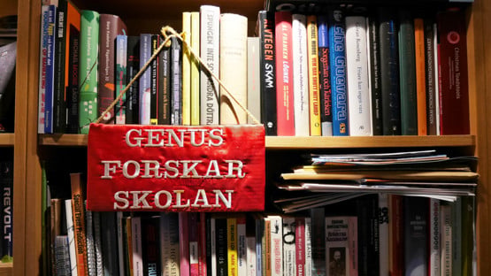 Broderad skylt där det står "Genusforskarskolan" hänger på en bokhylla
