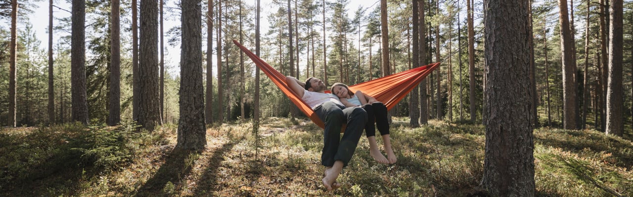 Pappa och flicka vilar i hängmatta i skogen.