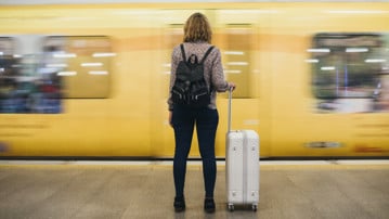 Kvinna står på en perrong med väska medan ett tåg åker förbi i hög fart.