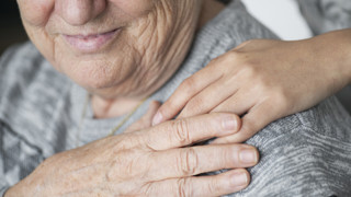 Detalj av en yngre person som lägger sin hand på en äldre kvinnas axel.