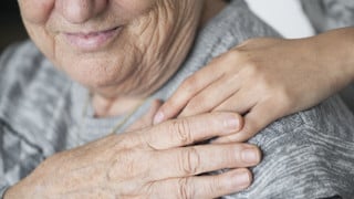 Detalj av en yngre person som lägger sin hand på en äldre kvinnas axel.