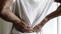 Person med ont i ryggen som trycker sina händer mot ryggen.