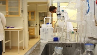 Interiörbild från Miljöarkeologiska laboratoriet med flaskor i förgrunden och en man i vit labbrock i bakgrunden