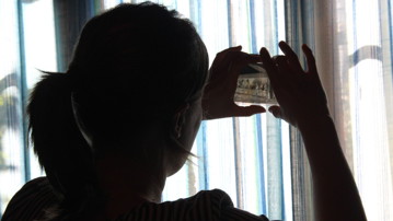 Jenny Ingridsdotter ute hos informant fotograferar ut ur ett fönster och bilden är tagen i motljus.