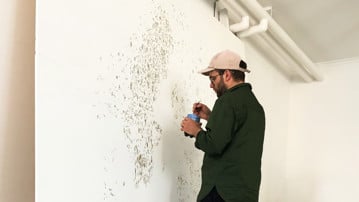 A man is painting with tar on a canvas, and a toddler is watching in the foreground