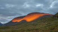 Solen lyser på ett berg i svenska fjällen.