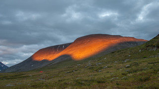 Solen lyser på ett berg i svenska fjällen.