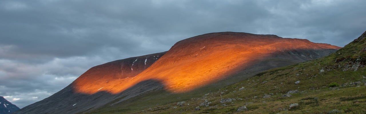 Solen lyser på ett berg i svenska fjällen.