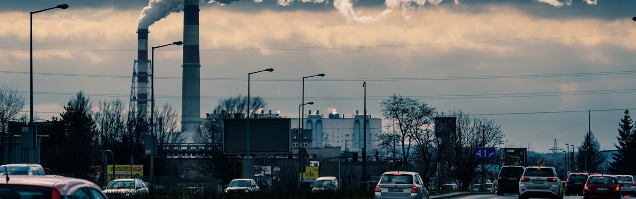 Bilar och rök från skorstenar i industriområde.